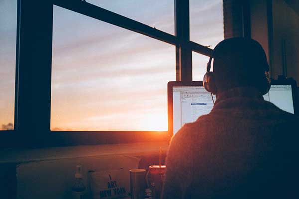 man using laptop with sunset through window