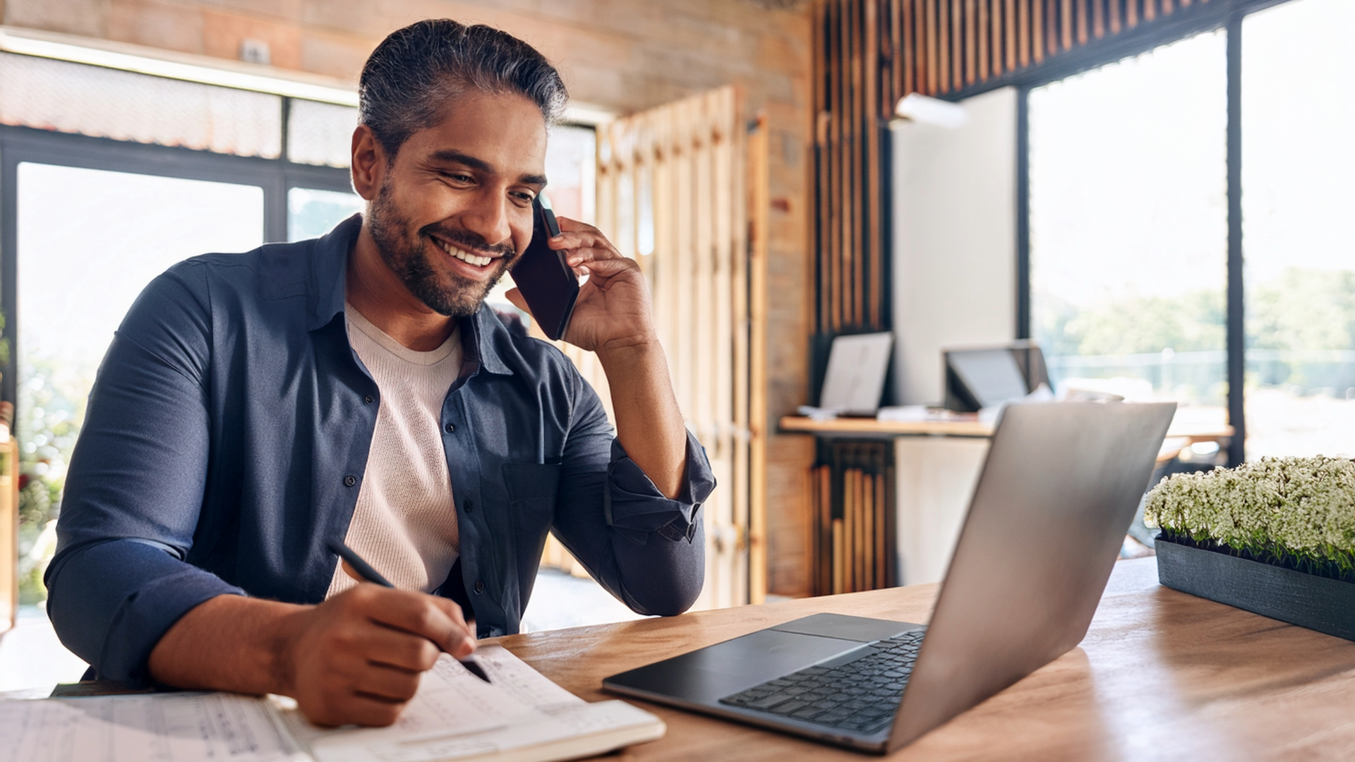 male talking on phone as he is sitting at a desk with a computer 