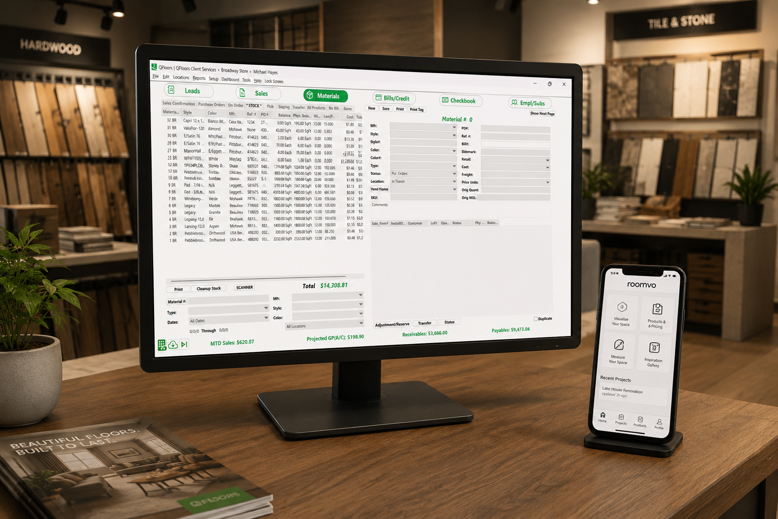 QFloors screen on a wood desk with a mobile phone with the Roomvo RSA app next to it in a flooring showroom.
